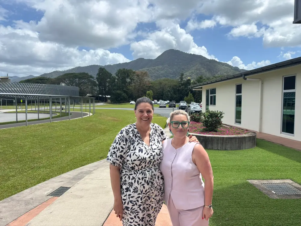 The two Amandas: Amanda from RollCall with Amanda from one of our Cairns schools, outside a school building with green hills behind them.