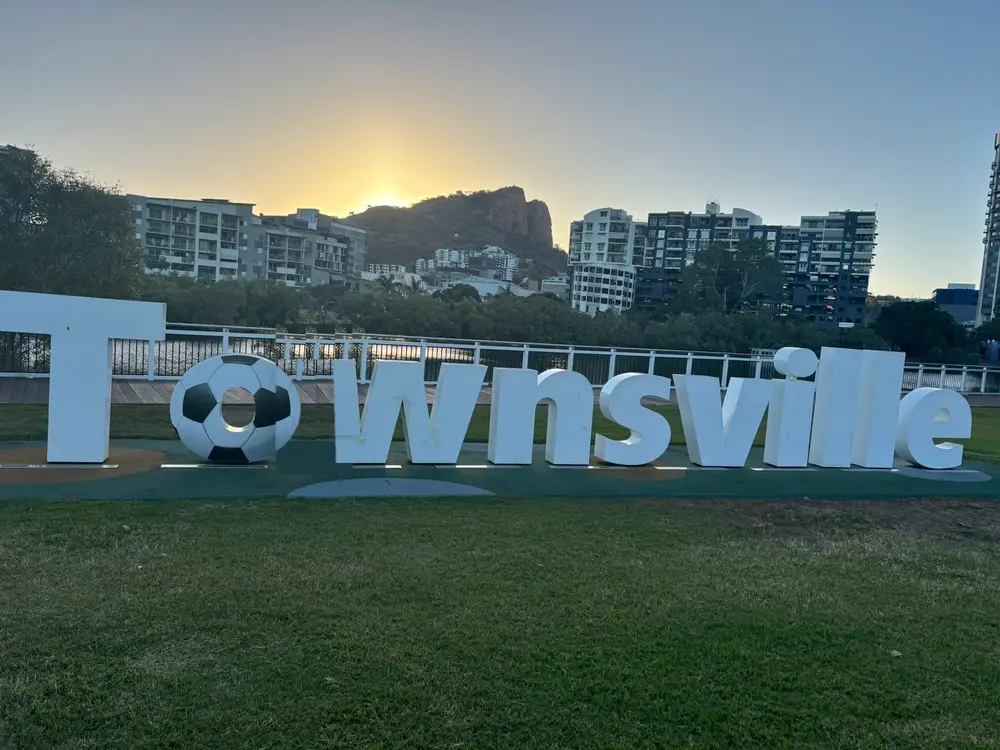 The giant white Townsville sign on the waterfront at sunset, with Castle Hill behind it.